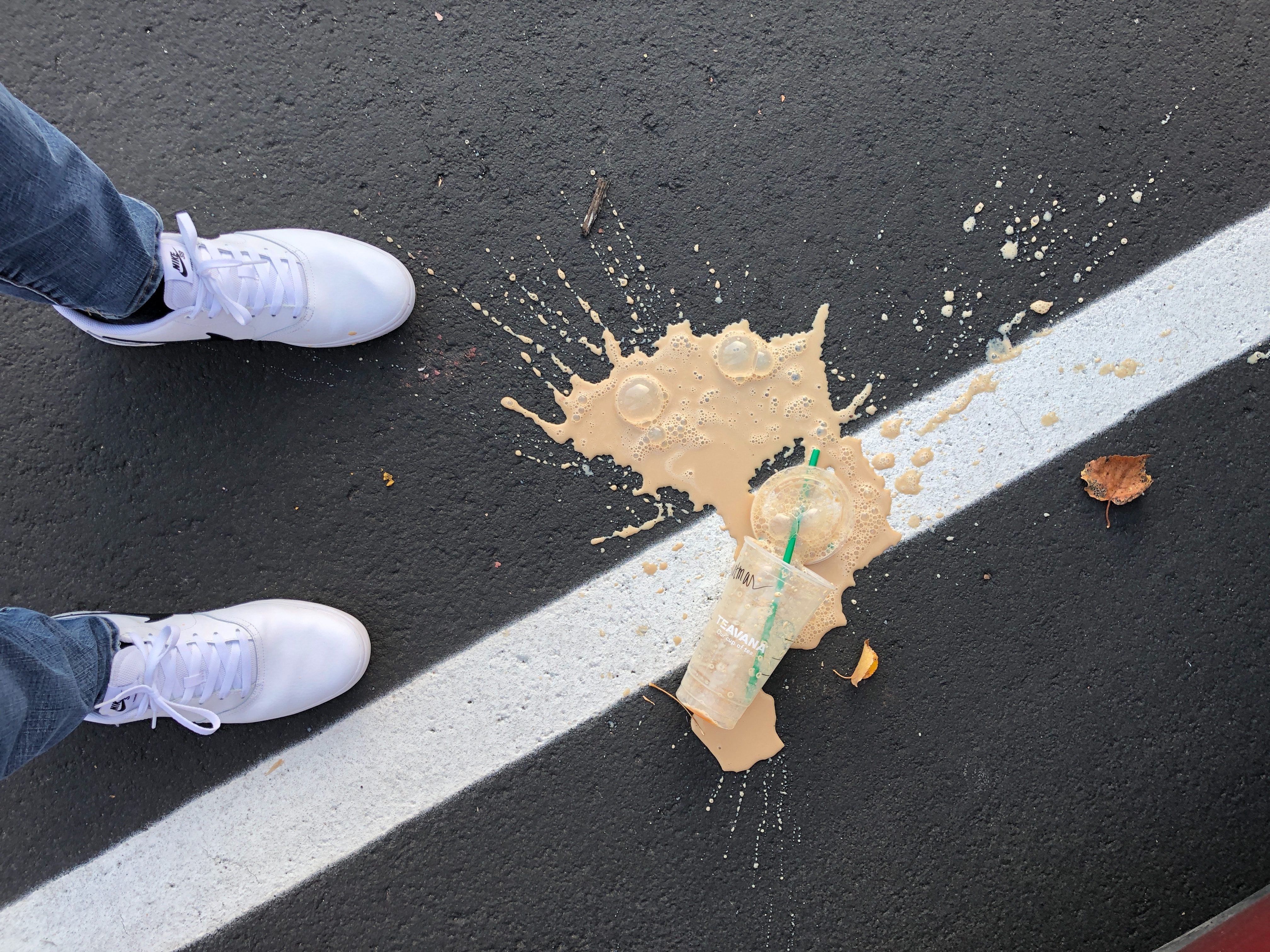 Coffee spilled on the ground in a parking lot by viewer's feet.