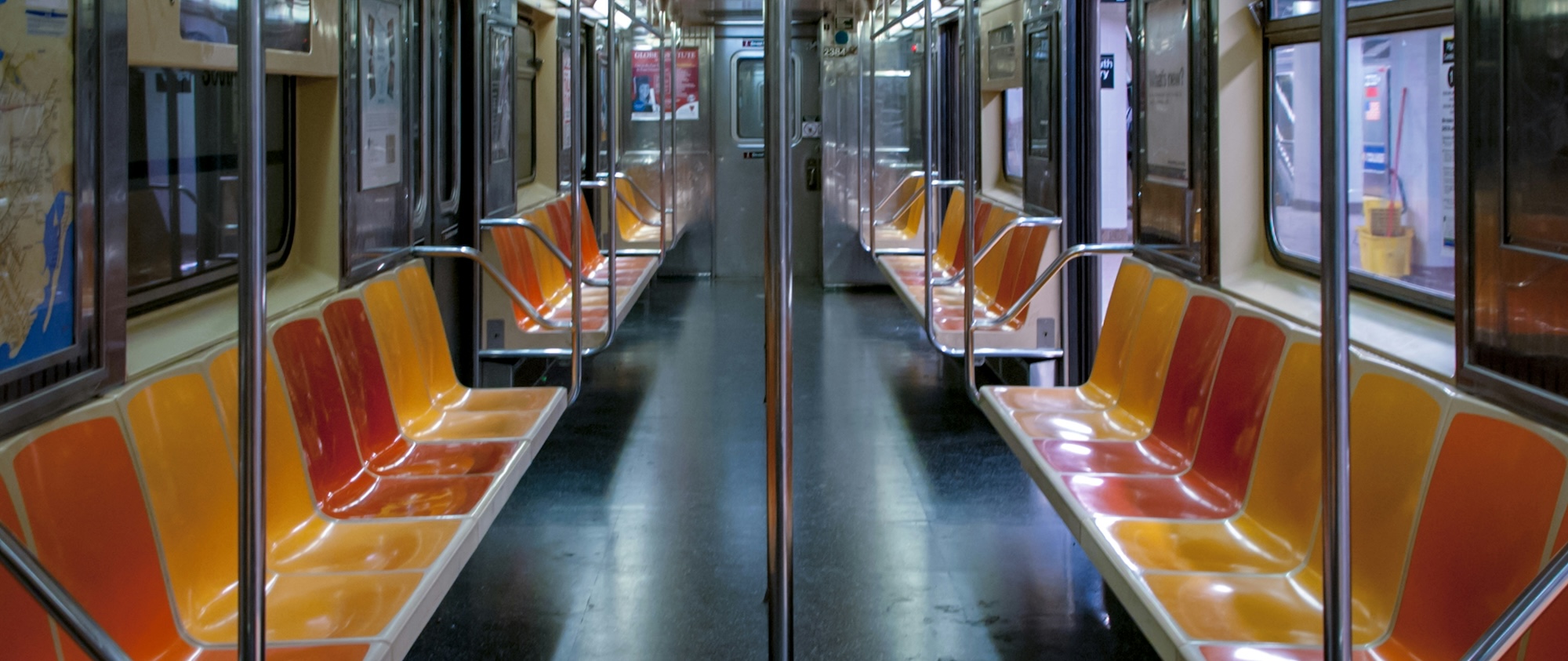 Interior view of an empty New York City subway car with red and yellow seats.